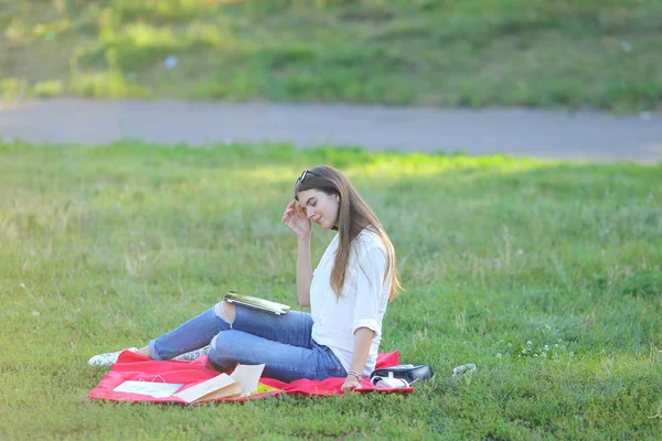 Young girl sitting on grass in the park works at a laptop and eating fast food