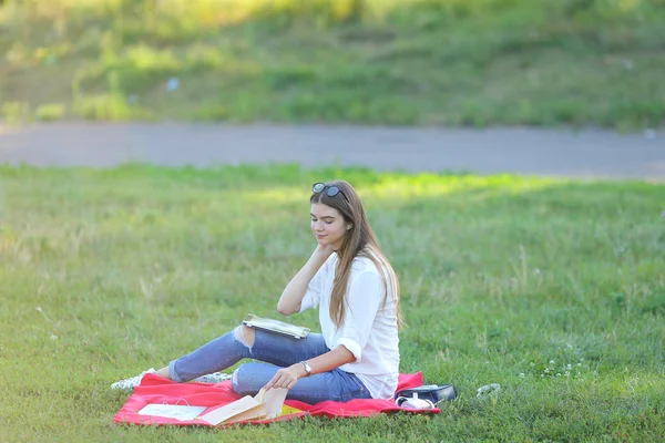 Young girl sitting on the grass in park works at a laptop and eating fast food