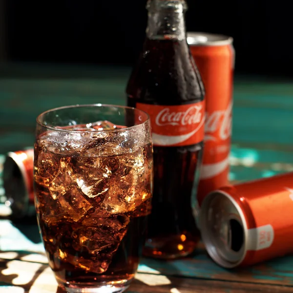 MINSK, BELARUS-AUGUST 25, 2016. Can and a glass of iced Coca-Cola on a wooden table