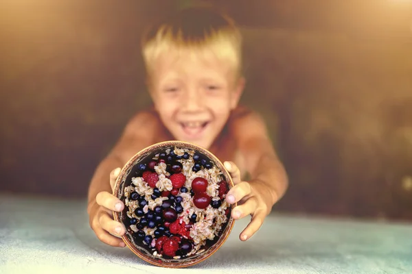 A boy holds up a plate of porridge with fresh fruit. Focus on the plate of porridge. Toning.