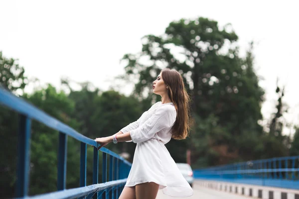 Beautiful girl stands on a bridge and looks at the sky. on the background of the river.