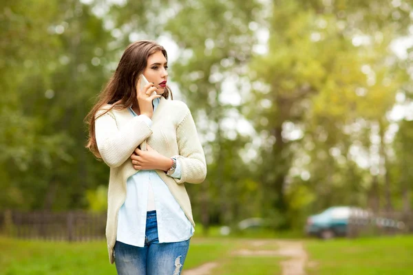 Girl in a white jacket, blue shirt and blue jeans, call on the phone and looking away