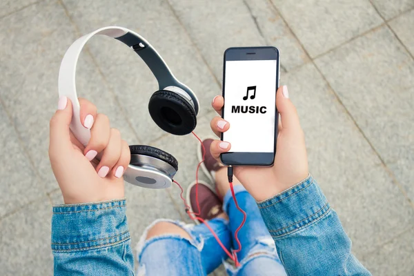 Hands of a young girl holding headphones and phone . On the phone says \