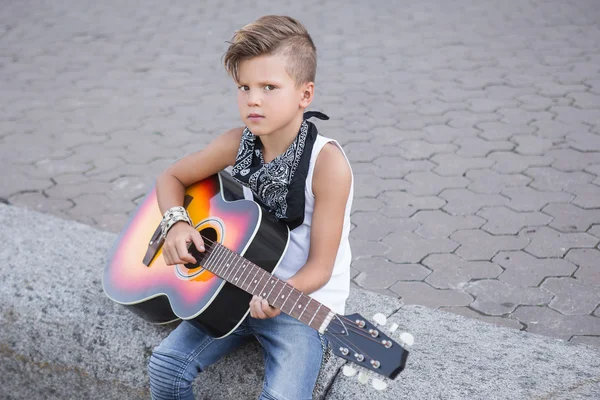 Stylish little boy learns to play the guitar . He dressed stylishly and he has cool hair