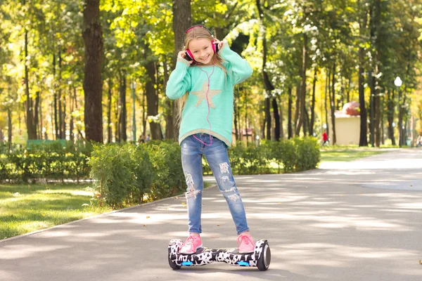 Girl rides on mini Segways in the headphones . She is happy and smiling