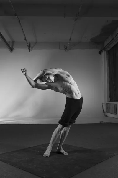 Young stong man dancing in the studio. Flexible body.Black and white.Full length. Side view
