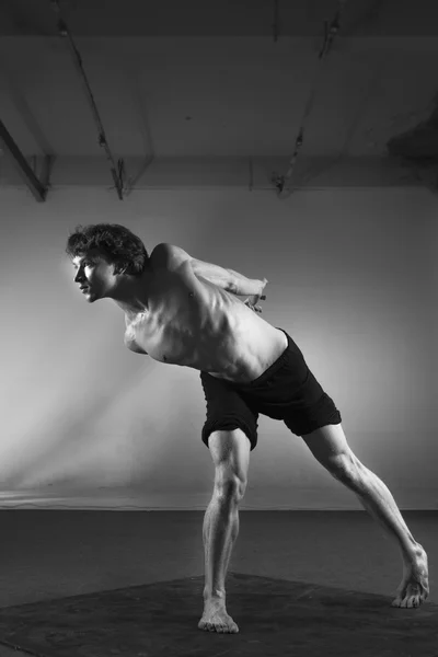 Young stong man dancing in the studio. Flexible body.Black and white. Full length. Side view