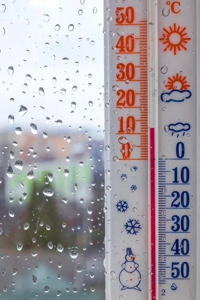 Rain drops on window glass and thermometer in summer day
