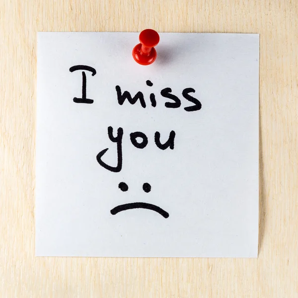 I miss you note on paper post it pinned to a wooden board