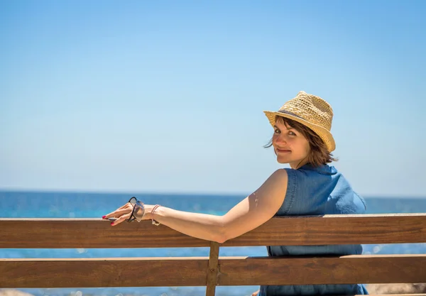 Pretty young woman sitting alone on a bench in front of the sea