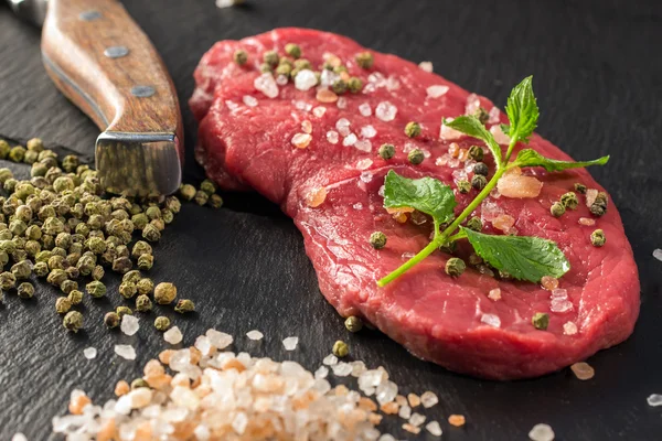 Raw Irish Sirloin Beef Steak on a slate stone board ready to be roasted with rosemary, chili pepper and salt