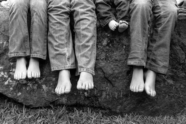 Legs and feet of siblings sitting on rock