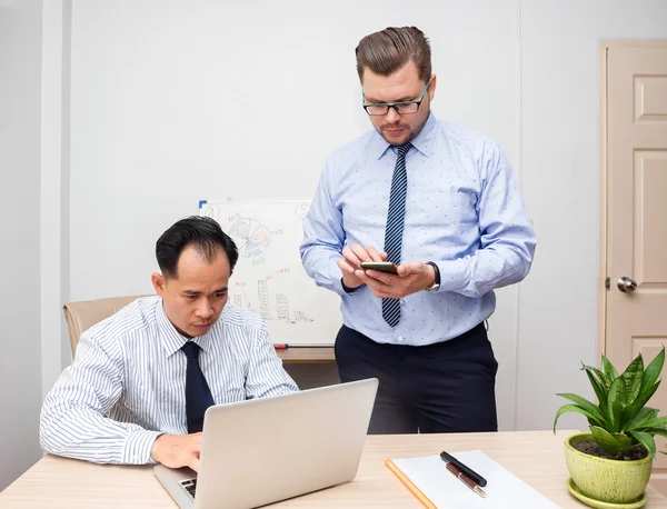 Two businessmen in office research with laptop and phone