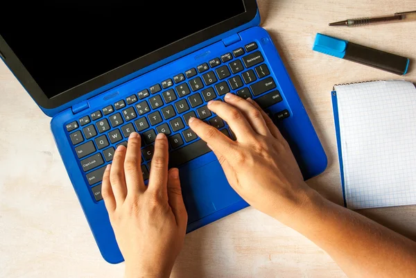 Hands of woman on the keyboard of her blue laptop