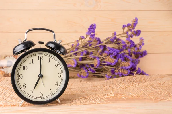 Black alarm clock and violet flower on the wood background