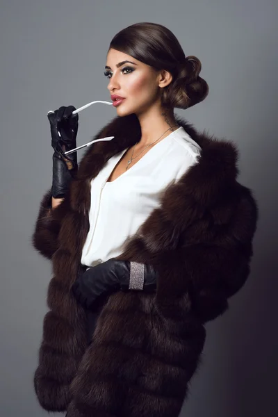 Glam model with provocative make up wearing white blouse, sable coat, leather gloves and set of luxurious bracelet, ring and chain with pendant.