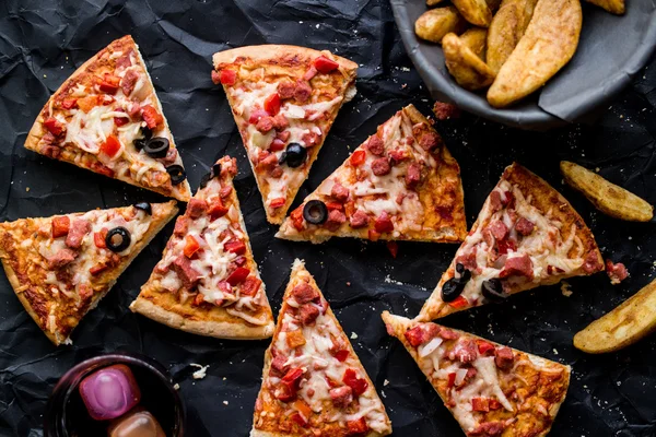 Pizza slices with potato wedges , nuggets and beverage on a black surface (Fast food concept)