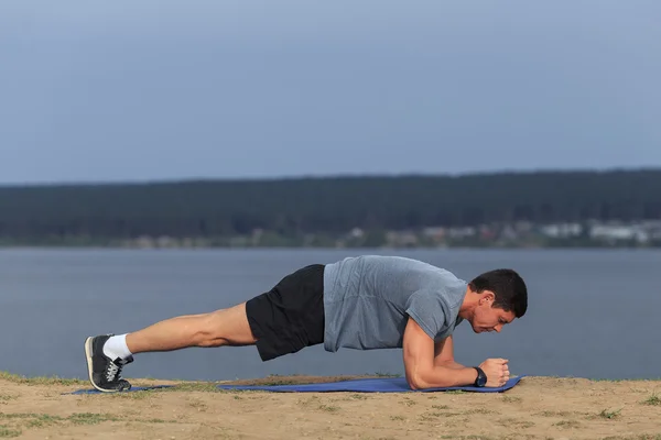 Crossfit training fitness man doing plank core exercise working out his midsection core muscles. Fit male fitness instructor planking exercising outside in summer.
