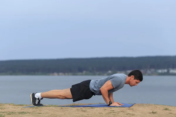 Young muscular man doing push-ups outdoors.