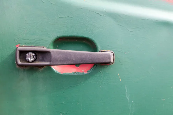 Close up of a black plastic car door handle. The vehicle door is green and there is red underneath the paint.