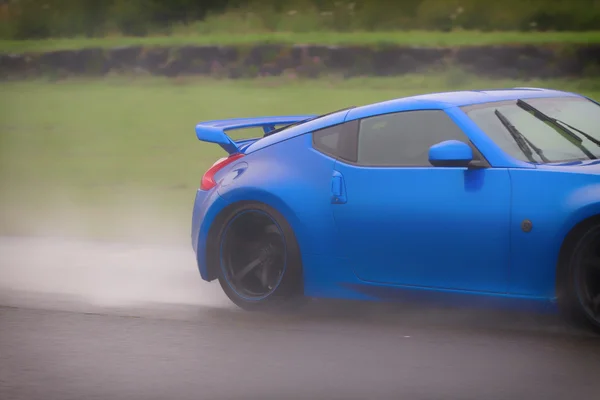 Speedy blue fast car in a spray of mist and rain water