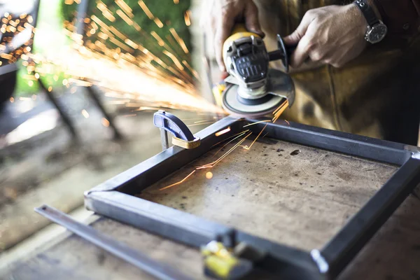 Custom furniture worker grinds welding seams on steel.
