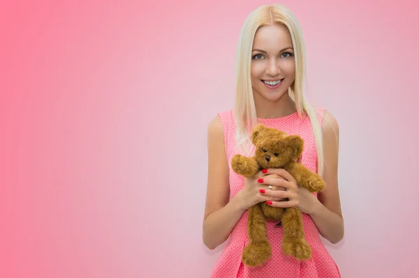 Delightful and charming blonde posing in a pink dress holding teddy bear