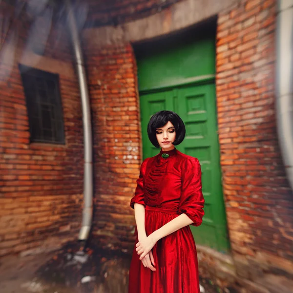 Young brunette girl in vintage romantic red dress near the door