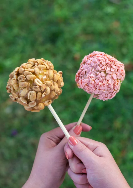 A woman hands holding candy apples with peanut butter, strawberry chocolate and peanuts on a autumn grass background