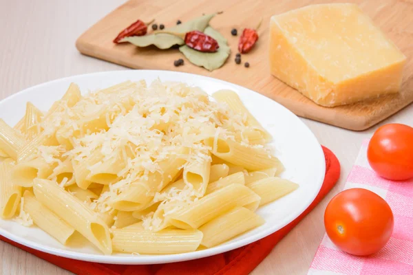 Penne pasta with grated cheese on a white round plate next to the spices and tomatoes on the table