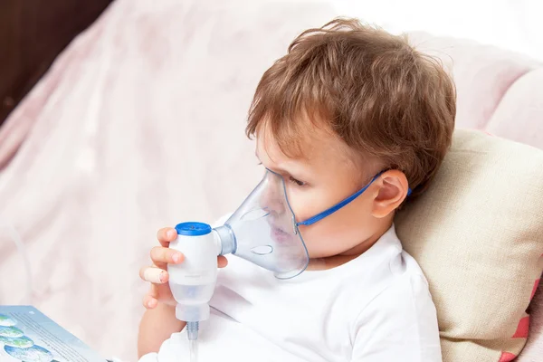 Boy making inhalation with a nebulizer at home and watching a book