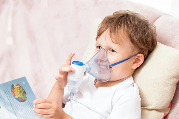 Boy making inhalation with a nebulizer at home and watching a book