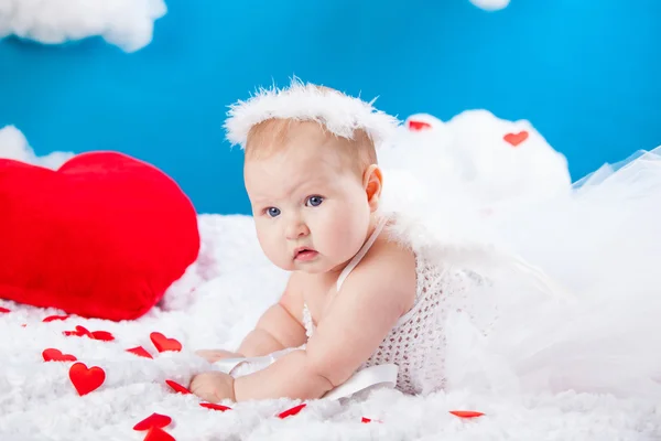 Baby angel in white dress with wings and a halo, lying in a cloud around him red hearts