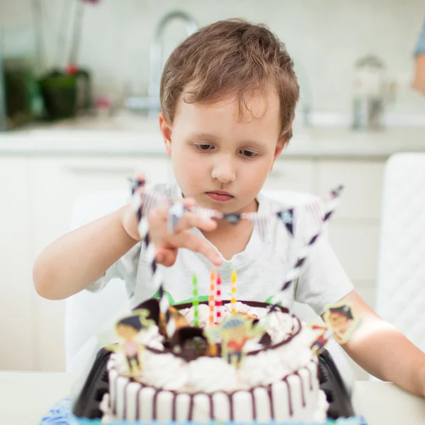 The boy blows out the candles on the cake at the table