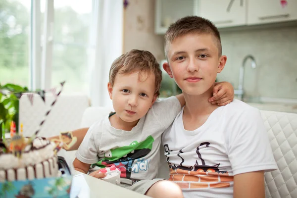 The brothers sit in an embrace on the kitchen table with a birthday cake