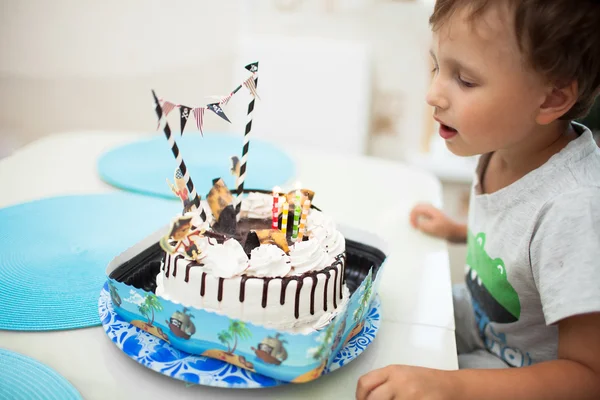 The boy blows out the candles on the cake at the table