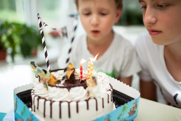 The boy blows out the candles on the cake at the table