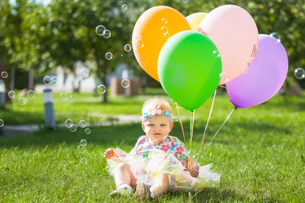 The child sits on the lawn with balloons and soap bubbles
