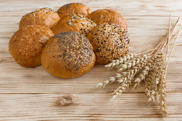 Bread loaf baguette roll lies on the ears of wheat on wood background.