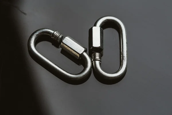 Two metal carabiner clip on a dark background