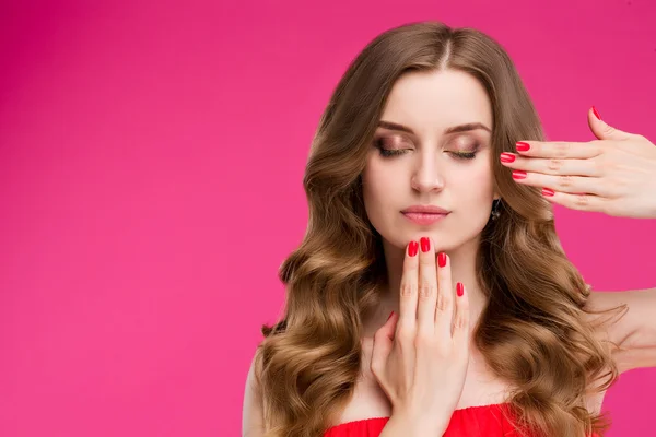 Stylish beautiful woman portrait with bright red nail Polish and fashion makeup, long curly hair shiny. Beauty, fashion, skin care, hair, shampoo. Isolated on pink background.