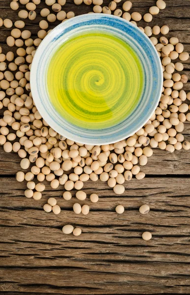 Soybean oil in ceramic bowl with soybean seed on wooden background