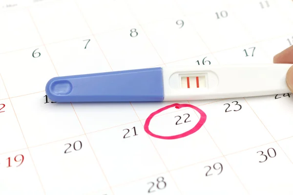 Pregnancy test with positive result lying on calendar