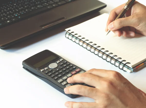Savings, finances, economy,technology and home concept, close upof hands with calculator counting and taking notes to notebook and laptop on white table, soft focus.