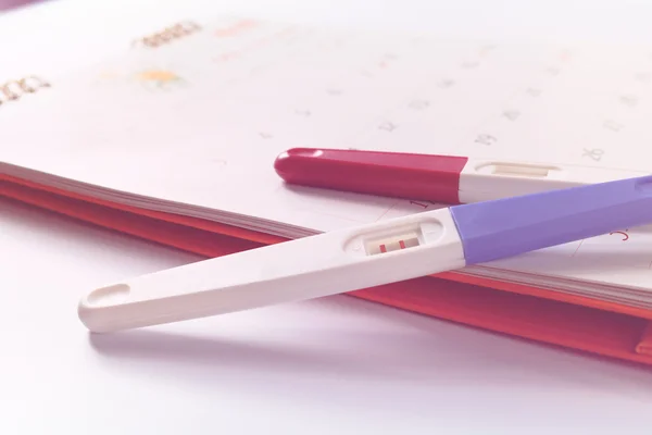 Pregnancy test with positive result lying on calendar background