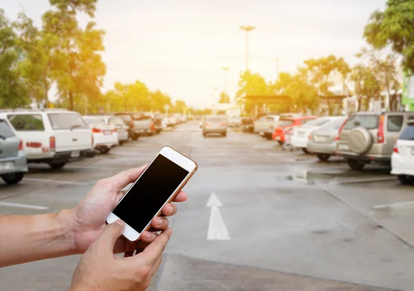 Human Holding Smart phone showing blank screen in man hand with blur cars parking