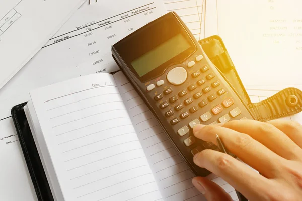 Savings, finances, economy and office concept. Business people counting on calculator, notebook, holding pen in hand, sitting at the table. Close up of hands and stationery, soft focus