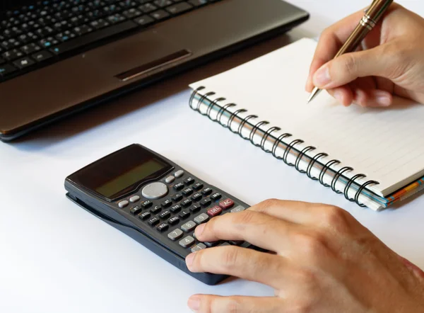 Savings, finances, economy,technology and home concept, close up of hands with calculator counting and taking notes to notebook and laptop on white table, soft focus.