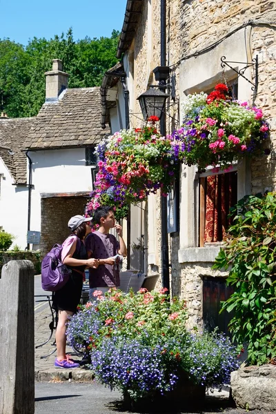 Tourists looking at the menu on the wall of The Castle Inn in the village centre, Castle Combe.