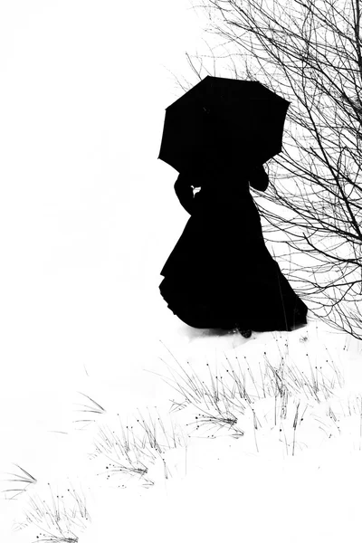 Woman in black walking up a hill with an umbrella - black and white photo, silhouette